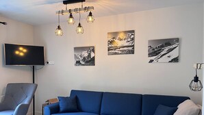 A modern living room with a blue sofa, a wooden coffee table, a grey armchair, and a TV mounted on the wall. - Quiet apartment in Cauterets with private parking (Cauterets)