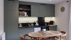 A modern kitchen with grey cabinets, a microwave, a coffee maker, and a dining area with a wooden table and chairs. - Quiet apartment in Cauterets with private parking (Cauterets)