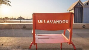 A red bench with "LE LAVANDOU" text, located outdoors with a clear sky and a building in the background.