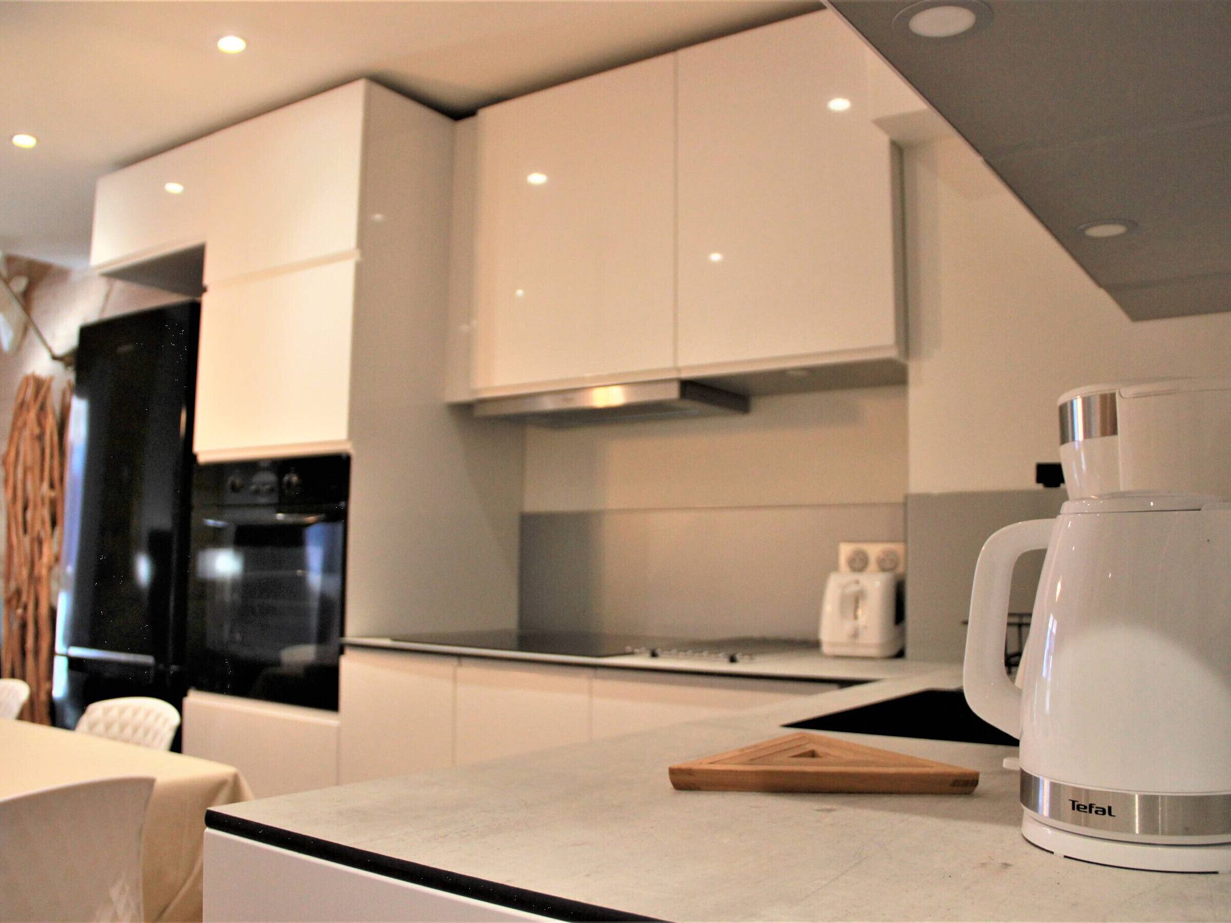 A modern kitchen with white cabinets, a black oven, a white coffee maker, and a wooden cutting board.