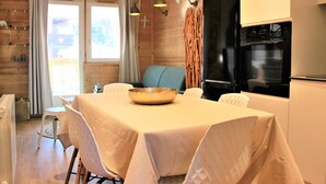 Un coin repas avec une table dressée pour quatre personnes, un canapé et une cuisine équipée d’un réfrigérateur et d’un four noirs.