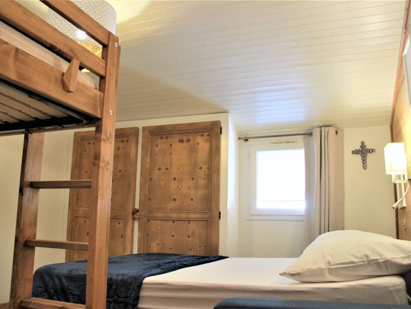 A bedroom with a bunk bed, wooden doors, a cross on the wall, and a window with curtains.