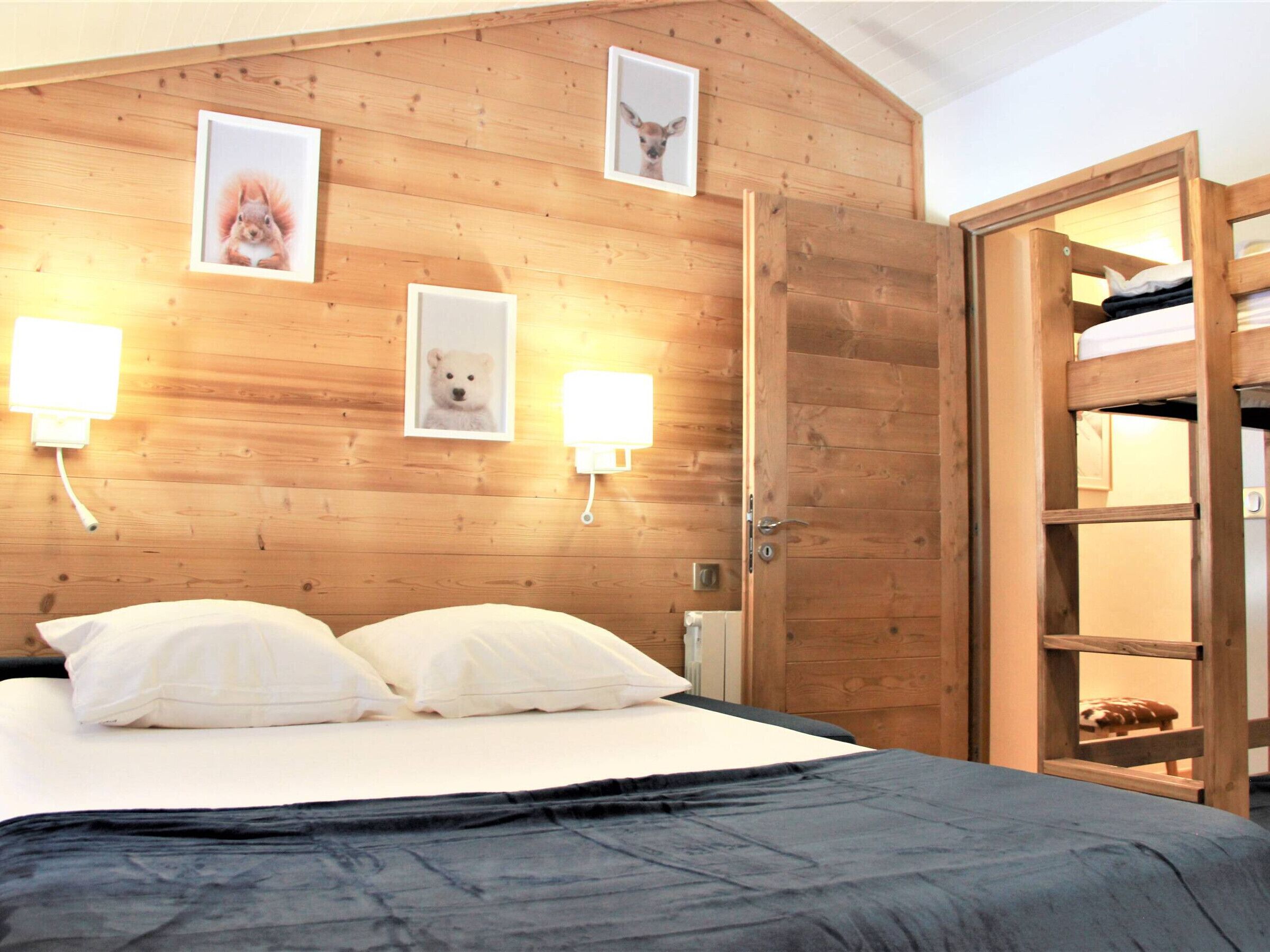 Een slaapkamer met houten lambrisering, een bed, twee wandlampen en een houten garderobe.