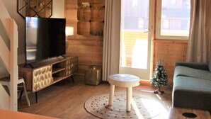 Un salon chaleureux avec un décor en bois, un téléviseur à écran plat posé sur un meuble en bois, une petite table ronde, un canapé vert et un sapin de Noël.