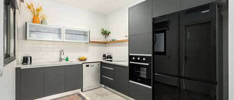 Una cocina moderna con armarios oscuros, horno empotrado y refrigerador negro.