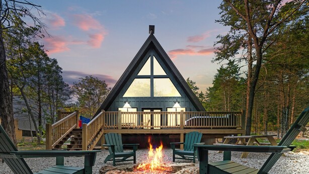 Eine Hütte mit einem Satteldach, einer Terrasse mit Stühlen und einer Feuerstelle.