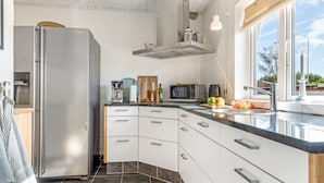 Una cocina moderna con un refrigerador de acero inoxidable, un microondas, una cafetera y un amplio ventanal que proporciona luz natural.