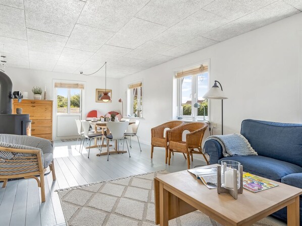 A spacious living area with a dining table, wicker chairs, a blue sofa, and a fireplace.