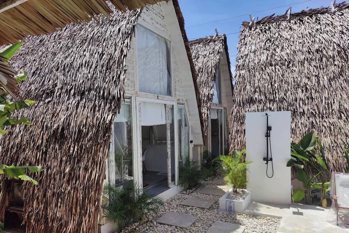 A modern house with a thatched roof, a glass door entrance, and a small garden area with stepping stones and plants.