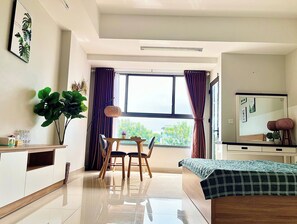 A modern bedroom with a bed, a desk with a chair, a large window with curtains, and a mirror.