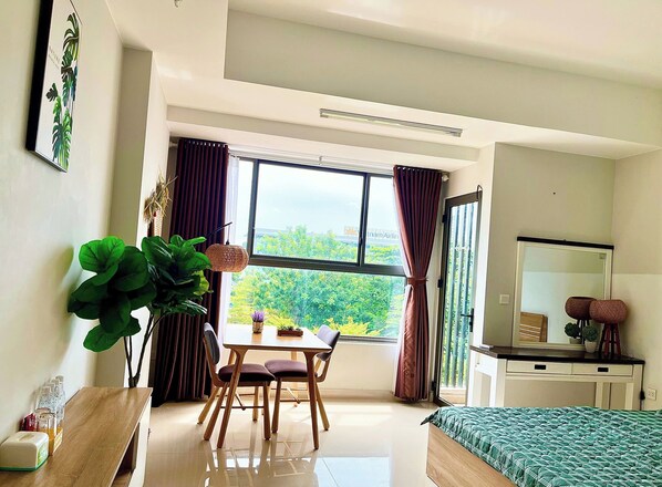 A modern bedroom with a large window, a bed, a desk, and a dining area.