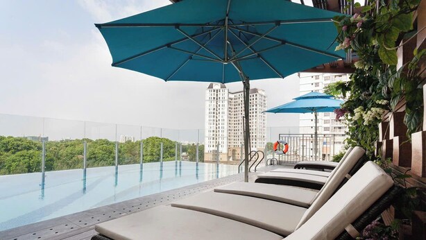 An infinity pool with lounge chairs and umbrellas, surrounded by greenery and high-rise buildings. - Nice Apartments near Tan Son Nhat Airpot (Ho Chi Minh City)