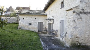 A stone building with a tiled roof, a small garden, and outdoor seating.