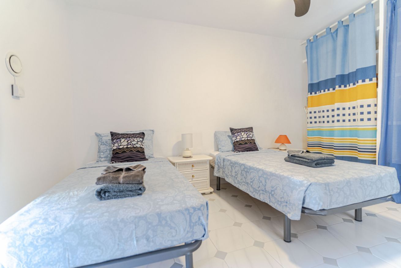 A hotel room with two beds, each with a patterned bedspread, a bedside table with a lamp, and a curtain with a striped pattern.