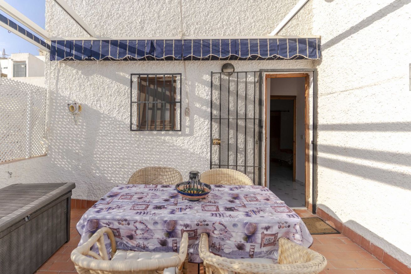 A patio with a table and chairs, a wicker sofa, and a covered area with a blue awning.