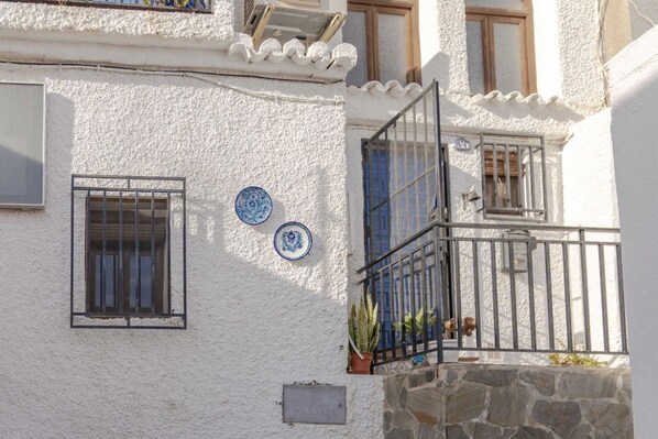 A building with white stucco walls, blue decorative plates, a stone base, and a metal balcony gate.