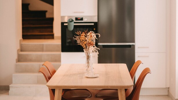 A modern kitchen with white cabinetry, a stainless steel refrigerator, and a dining table with wooden chairs.