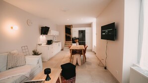 A modern apartment with a living room, dining area, kitchenette, and a TV mounted on the wall.