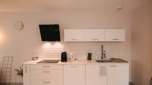 A modern kitchen with white cabinets, a black coffee maker, a kettle, and a sink.
