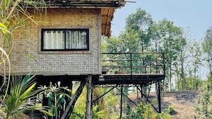 Eine rustikale Holzhütte mit Fenster und Balkon, umgeben von Grünpflanzen und Bäumen.