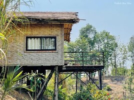 Una estructura de madera rústica con ventana y balcón, rodeada de follaje y árboles.