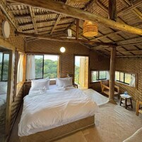 Un dormitorio amplio con una cama grande, dos ventanas con cortinas, techo de madera y una pequeña mesa con sillas.