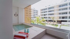 A modern hotel room with a large window, a private pool, and a view of the surrounding buildings and greenery.