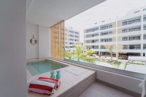 Habitación de hotel moderna con un ventanal grande, una piscina privada y vistas de los edificios y la vegetación circundantes.