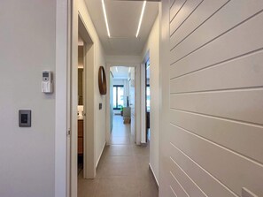 Un pasillo moderno con piso de color claro, techo con iluminación lineal y un termostato fijado a la pared.