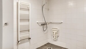 Ein Badezimmer mit weißen Fliesen, einem weißen Handtuchhalter, einer Dusche inklusive Duschbrause und einer Haltestange.