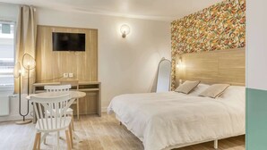 Ein Hotelzimmer mit Bett, Schreibtisch mit Stühlen, einem an der Wand befestigten Fernseher und einer Wanddekoration mit Muster.