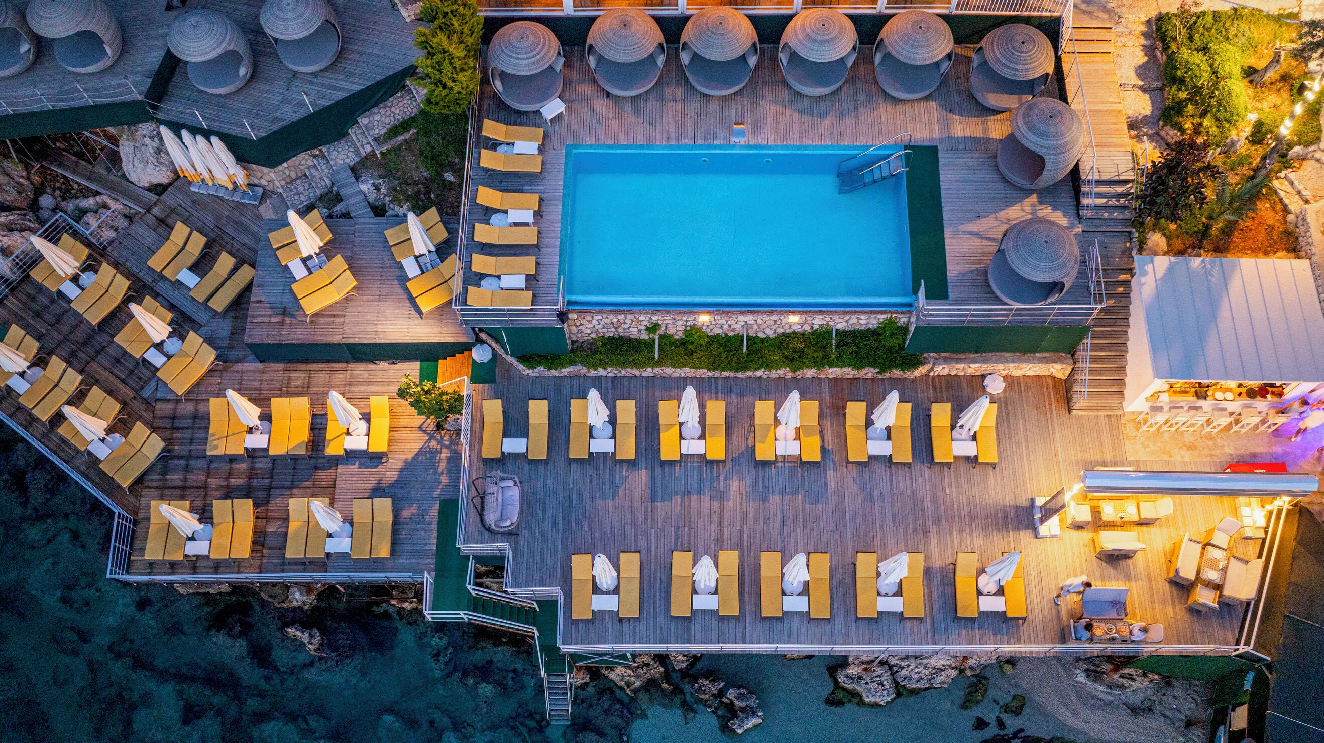 Vista aérea de la zona de la piscina de un complejo turístico, con múltiples tumbonas y una piscina central.
