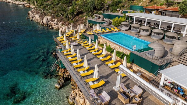 Ovenfra et kystresort med en klar swimmingpool, liggestole og udendørs siddeområder.