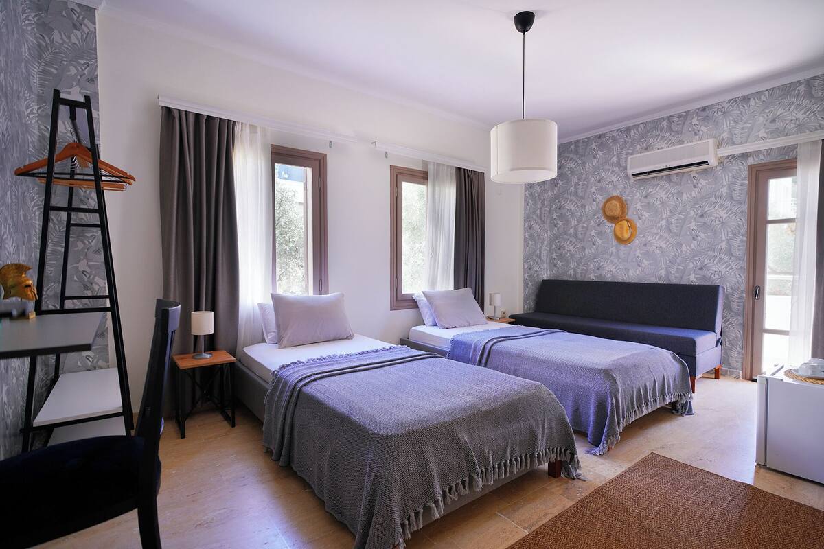 A hotel room with two beds, a desk with a chair, a ladder, and a hanging light fixture.
