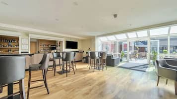A spacious bar area with multiple seating options, a television mounted on the wall, and a view of the outside through large windows.