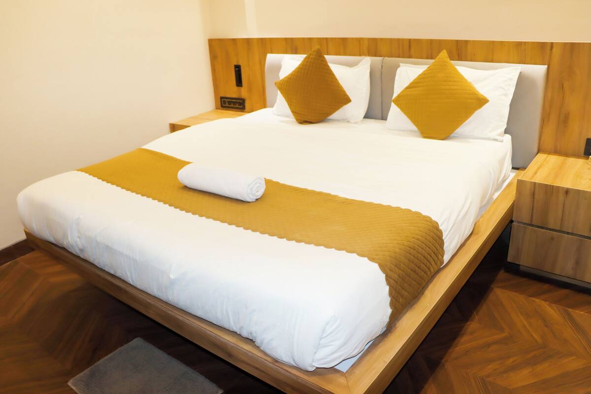 Ein ordentlich bezogenes Bett mit einem Holz-Kopfteil, einer weißen Tagesdecke und zwei senfgelben Kissen.