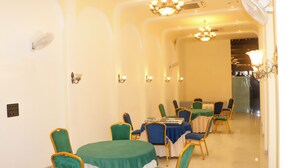 Un comedor con mesas redondas, sillas verdes y azules, y candelabros.