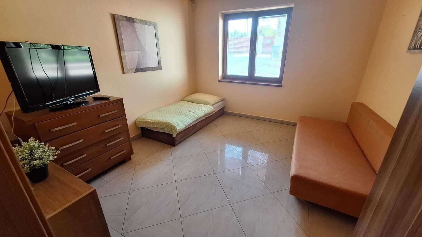 Een kamer met een bed, een bank, een televisie, een dressoir en een raam.