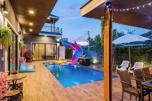 Un área de piscina moderna al aire libre con tobogán, sillones de descanso y una mesa de comedor.