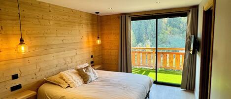 Een moderne slaapkamer met een groot bed, houten wanden en uitzicht op een houten terras en bomen.