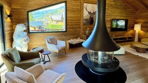 Ein gemütliches Blockhaus-Interieur mit Kamin, bequemen Sitzmöglichkeiten und einem großen Fenster mit reizvollem Blick.