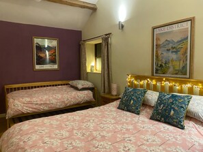 Een slaapkamer met twee eenpersoonsbedden, een groot bed met bloemenbeddengoed, een hoofdbord met lichtjes, een spiegel, een poster van het Lake District en een raam met gordijnen.