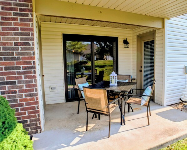 Une terrasse extérieure avec une table et des chaises, une porte-fenêtre coulissante et un mur en briques.