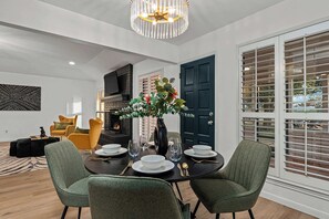 Een eetgedeelte met een tafel voor vier personen, een vaas met bloemen en een moderne kroonluchter.