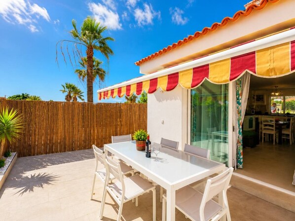 An outdoor patio with a white table and chairs, a wooden fence, and a palm tree.