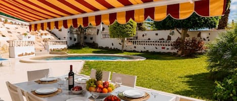 An outdoor dining area with a pool, white tablecloths, and a striped awning.