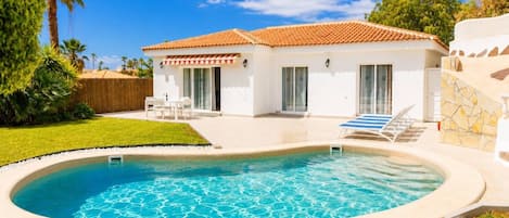 A residential property with a swimming pool, a patio with outdoor furniture, and a white building with a tiled roof.