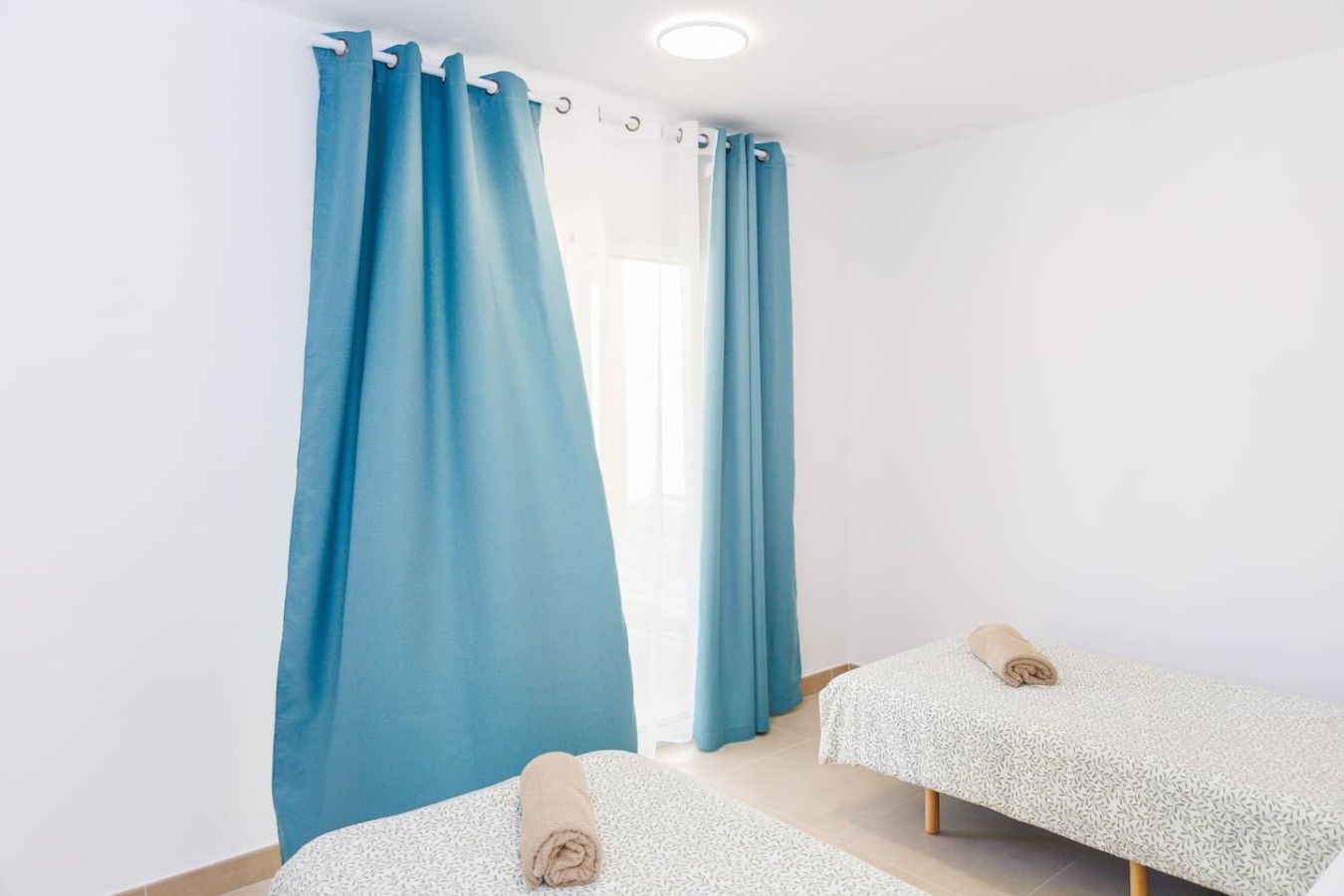 A room with two beds, a window with curtains, and a ceiling light.