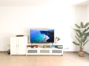 Un téléviseur à écran plat posé sur un meuble blanc, avec une image de plage en arrière-plan, un meuble blanc et une plante en pot.