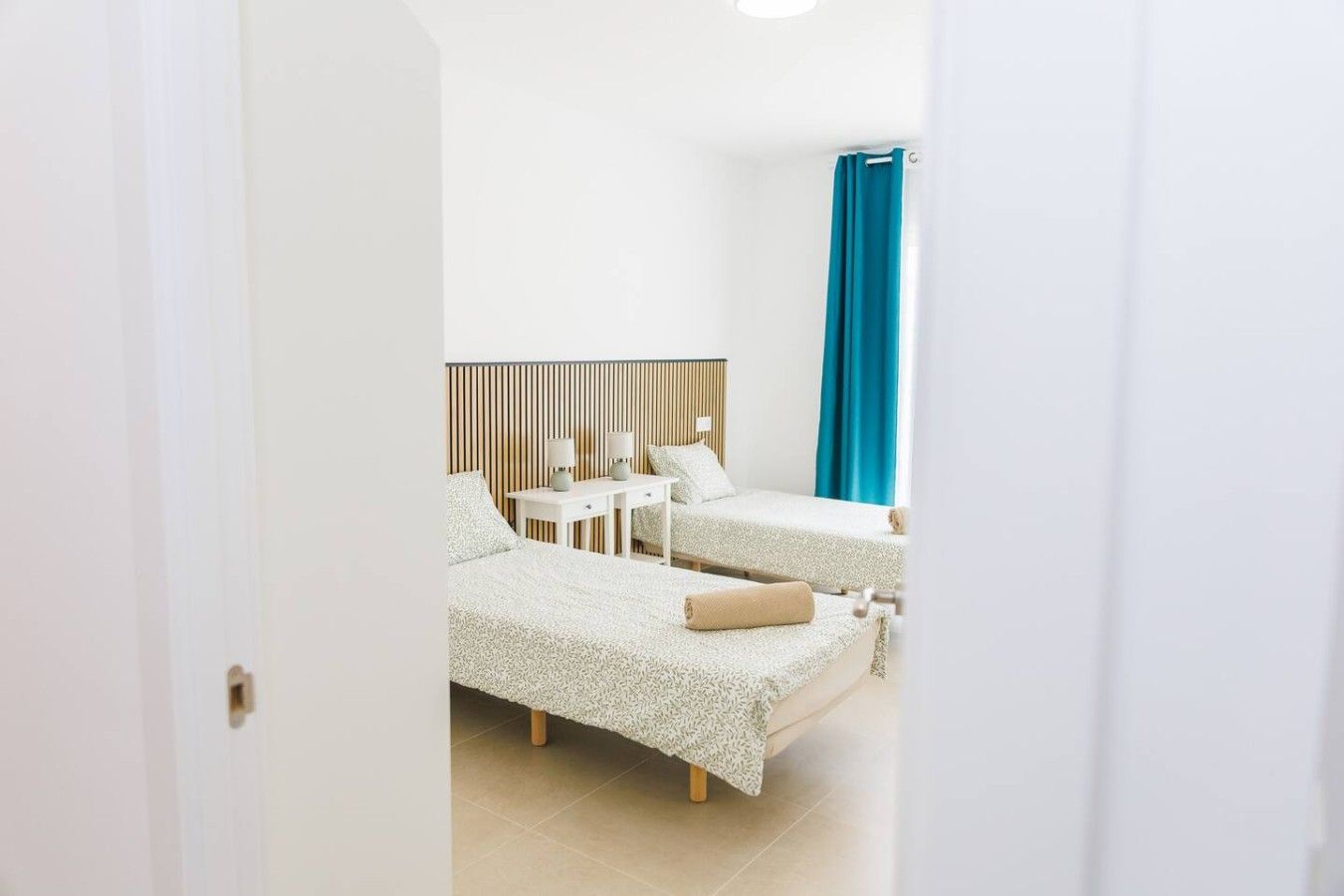 Quarto de hotel com duas camas, uma escrivaninha e uma cortina azul.